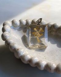 A clear resin rectangular charm with a gold foiur leaf clover and silver clasp sits inside a white ceramic bowl