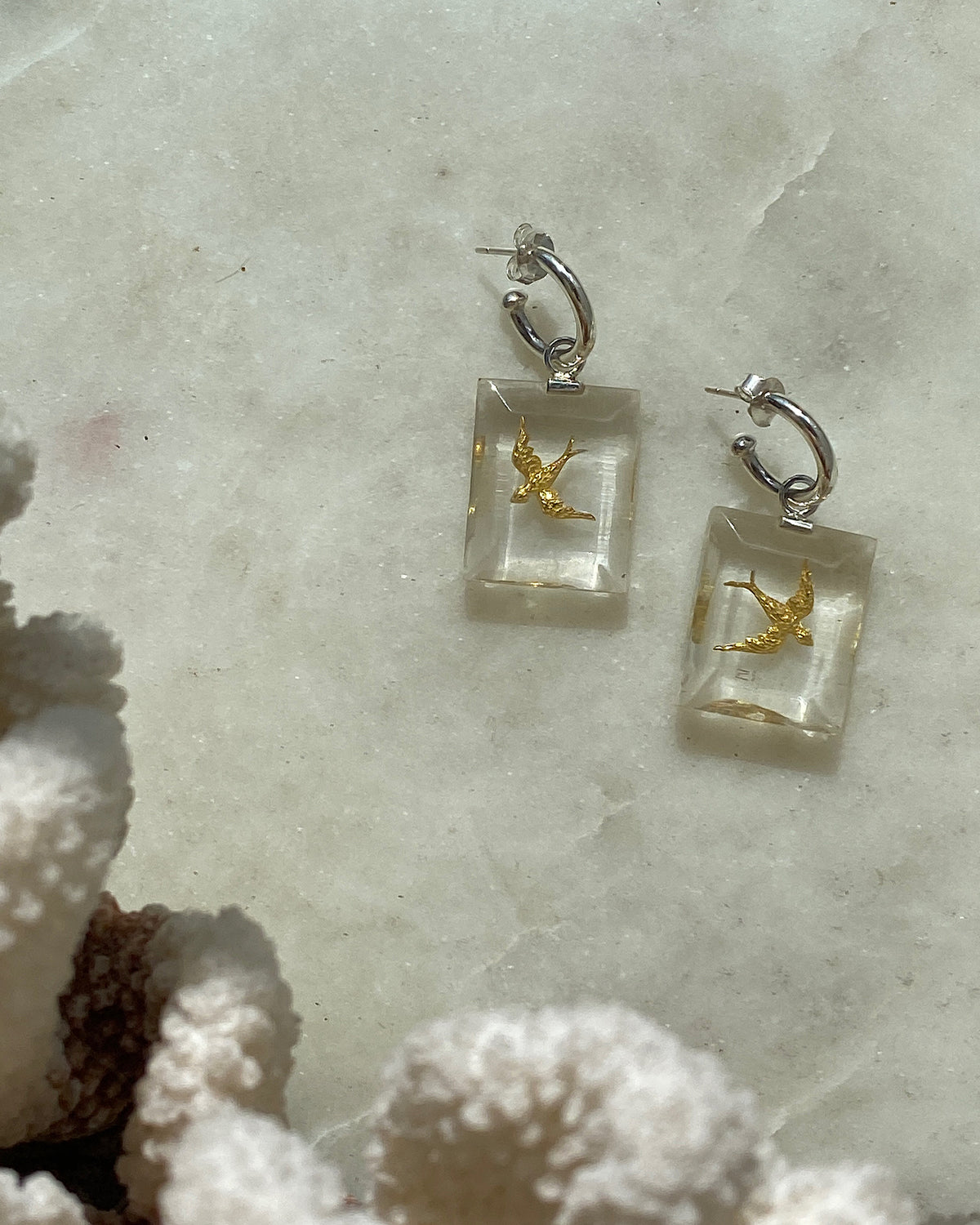 small gold swallow birds set into resin hang from a silver hoop earring