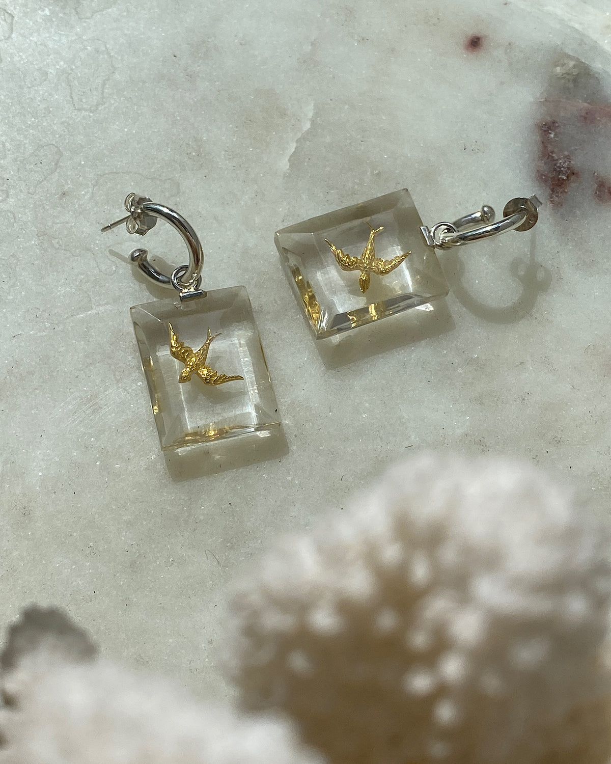 small gold swallow birds set into resin hang from a silver hoop earring on marble