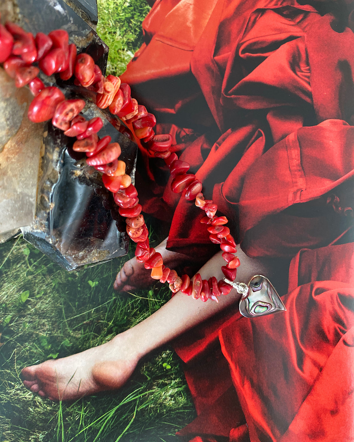 a red coral jagged necklace with a central abalone heart charm sits on a magazine page