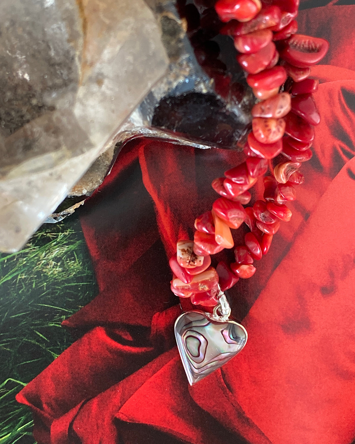 a red coral jagged necklace with a central abalone heart charm sits on a magazine page