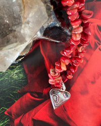 a red coral jagged necklace with a central abalone heart charm sits on a magazine page