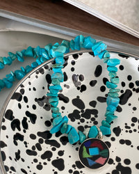 a turquoise jagged necklace with a central round multi colour and silver pendant sits in a bowl