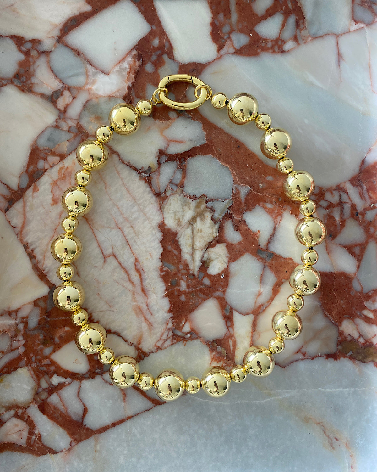 statement gold ball necklace sits on marble