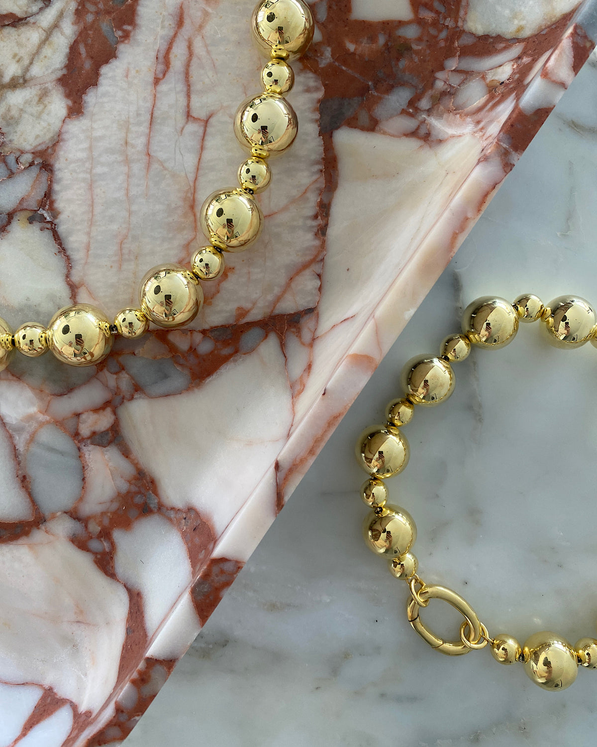 twio statement gold ball necklaces sit on marble