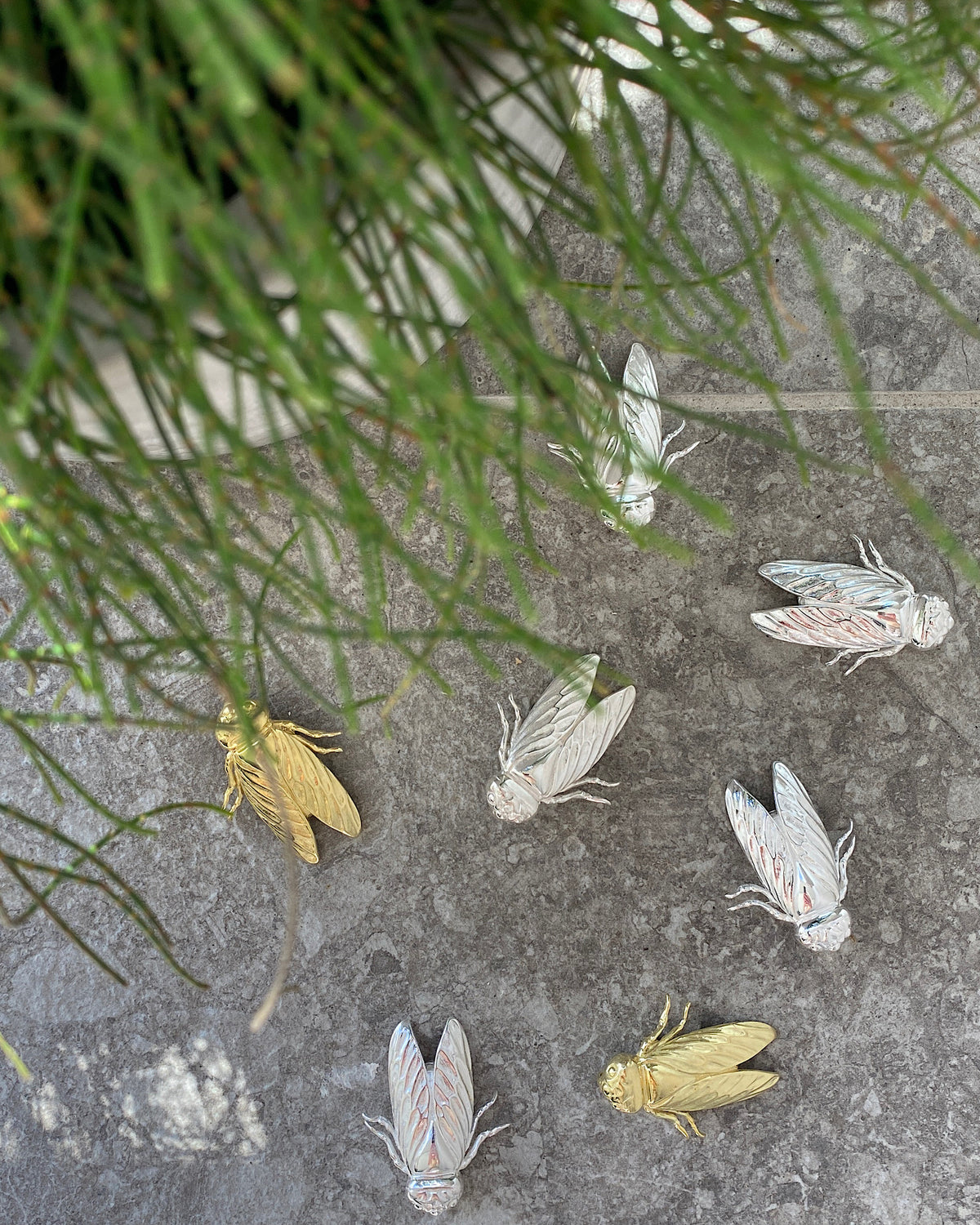 silver and gold cicada brooches with greenery in the foreground