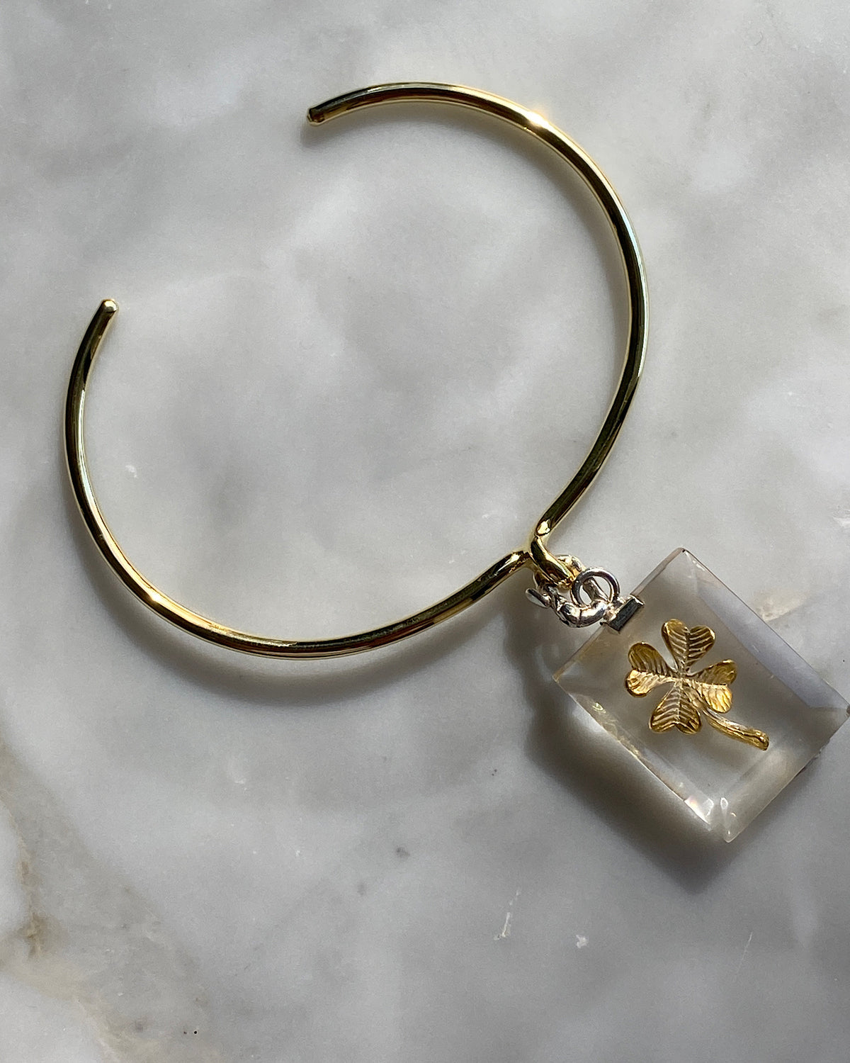 A clear resin rectangular charm with a gold four leaf clover and silver clasp is attached to a gold bracelet