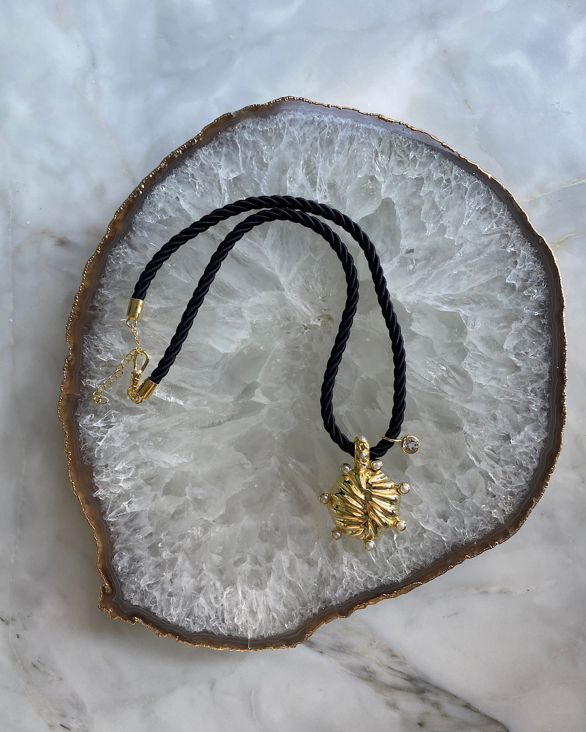 unusual striped gold pendant with pearls dotted around sit on a black cord pendant with a crystal