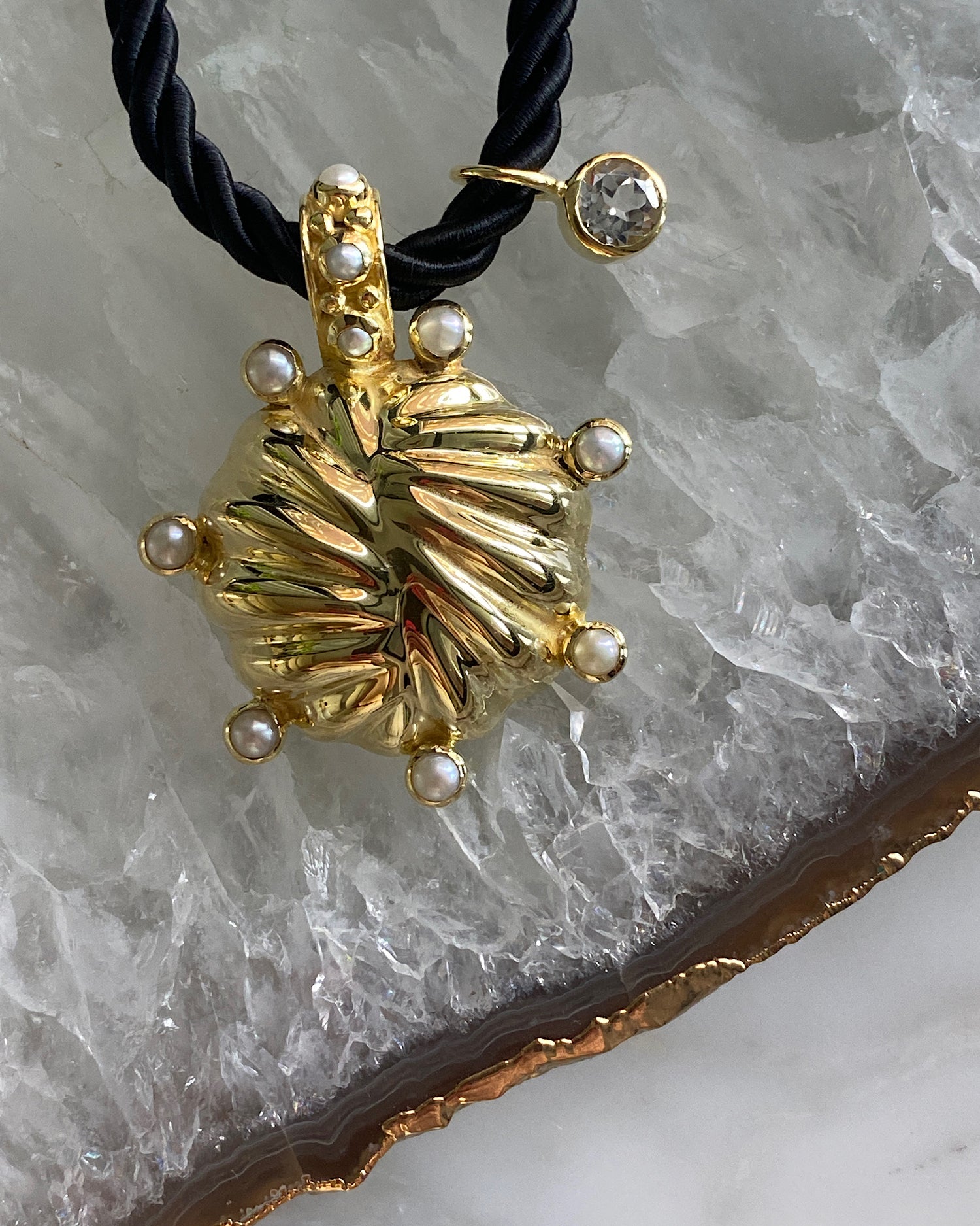 unusual striped gold pendant with pearls dotted around sit on a black cord pendant with a crystal