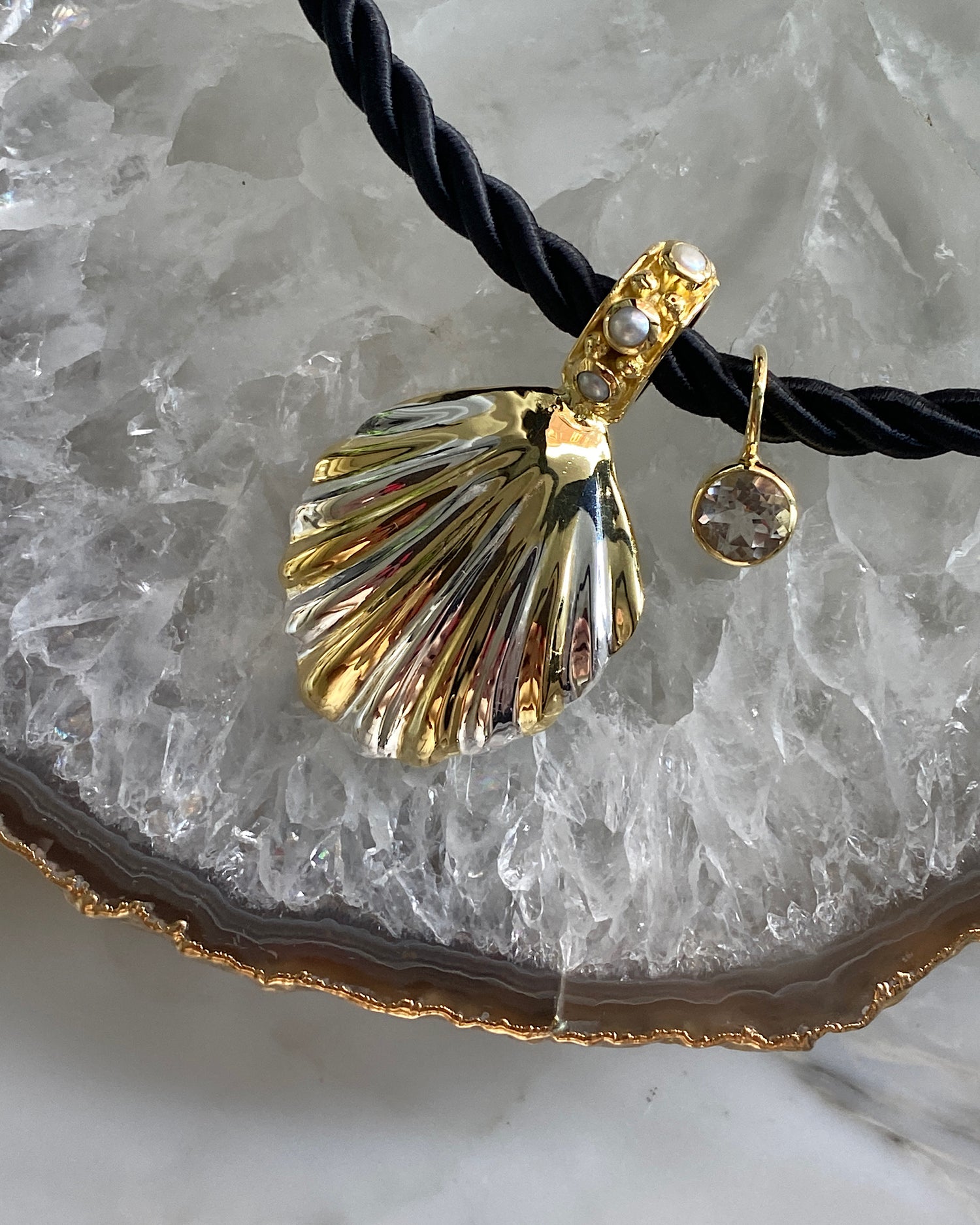 unusual striped gold shell pendant with pearls dotted around sit on a black cord pendant with a crystal