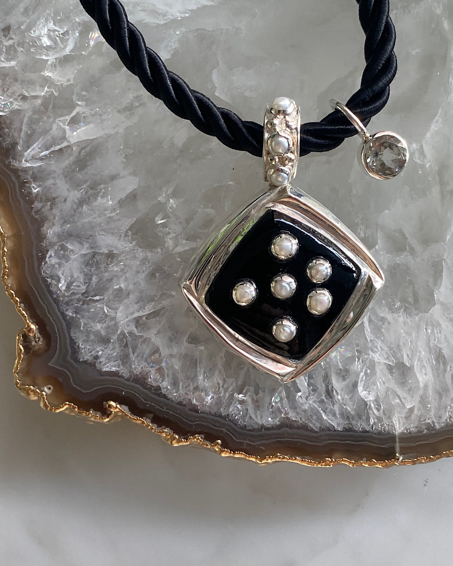 Inlaid black pendant studded with pearls sits on a black cord chain