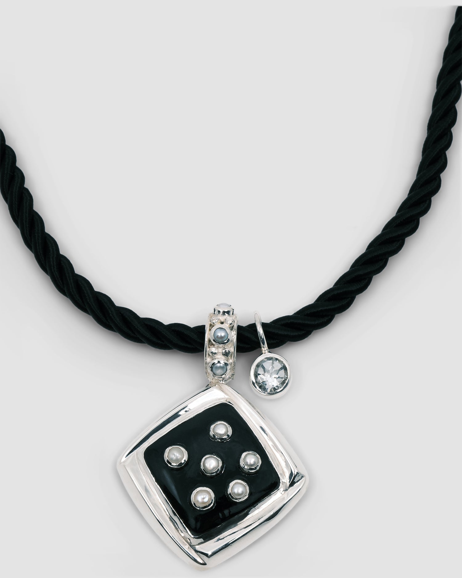 Inlaid black pendant studded with pearls sits on a black cord chain