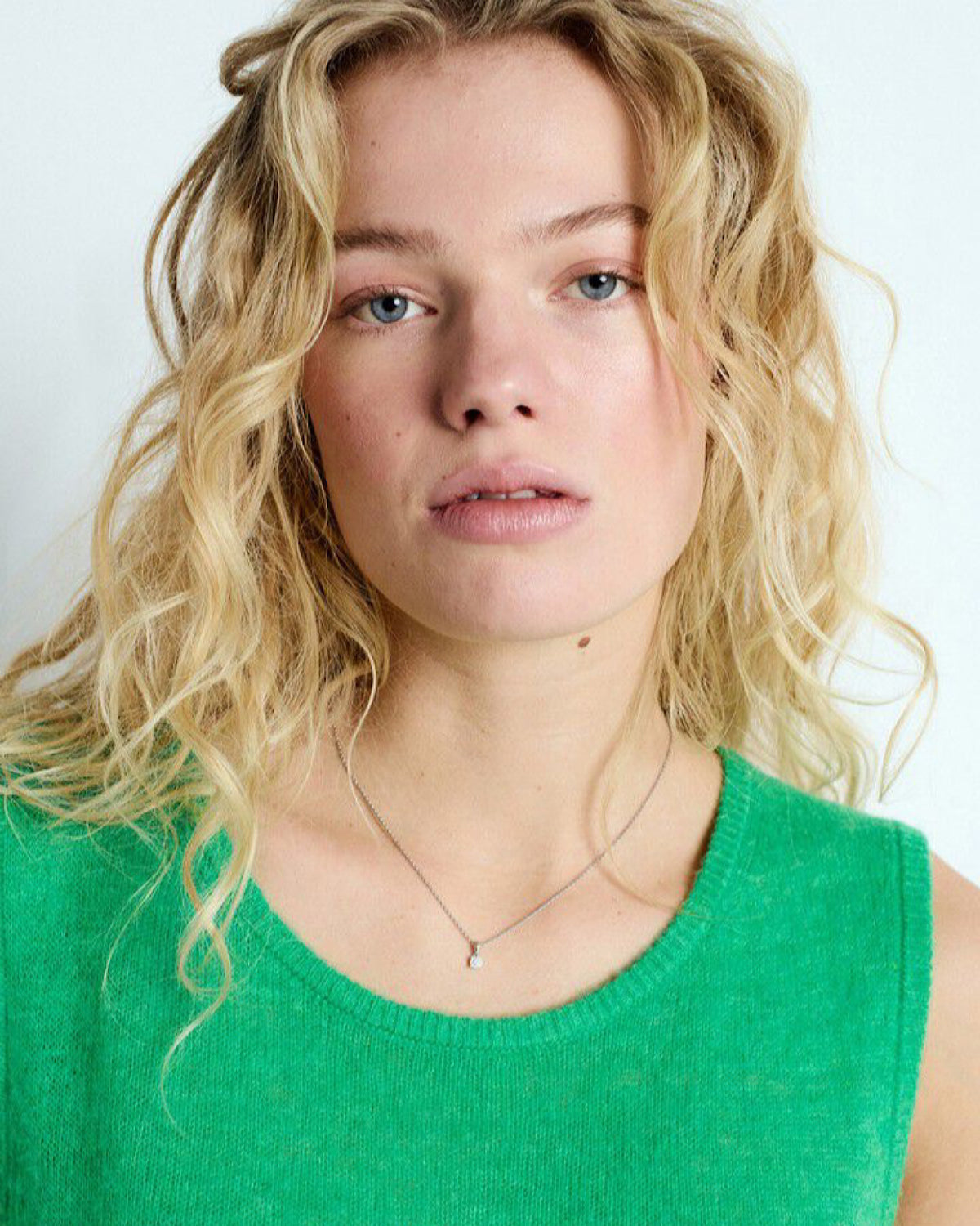 Person with blonde hair wearing a green top against a white background