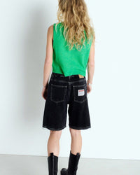 Person wearing a green sleeveless top from Amerian vintage and black shorts on a white background