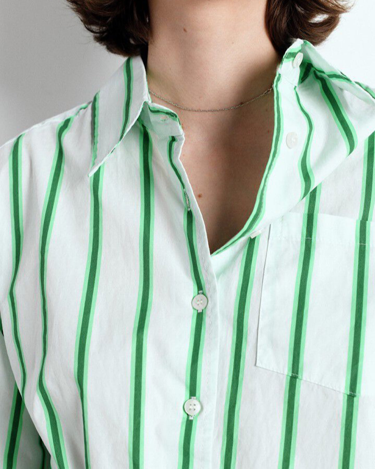 Close-up of a person wearing a white shirt with green vertical stripes.