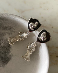 Silver ornate tassel and emu shield earrings sit in a bowl on marble background