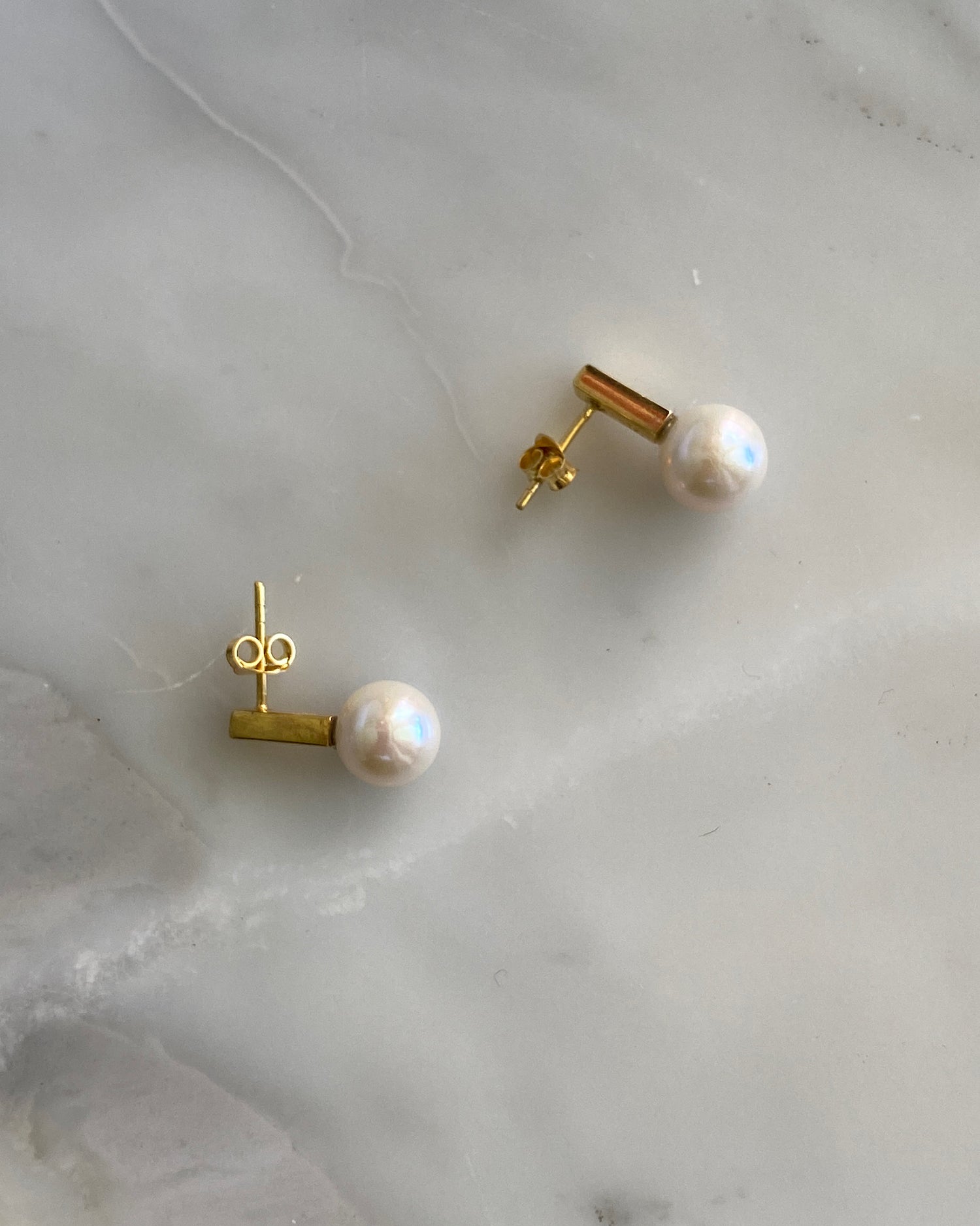 short gold bars with pearls attached sit on marble