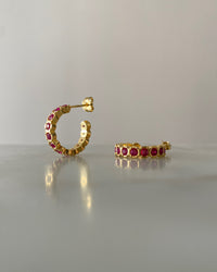 gold hoop earrings inlaid with red crystals sit on a reflective surface