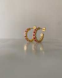 gold hoop earrings inlaid with red crystals sit on a reflective surface