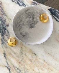 Gold rounded drop earrings with a latch closure sit in a b owl on marble