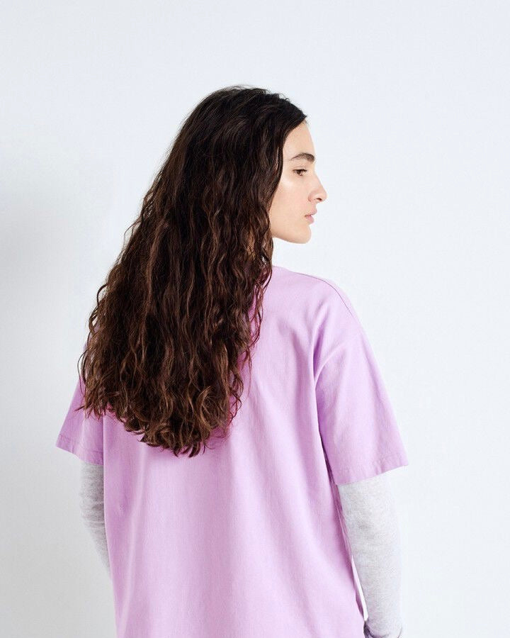 Person wearing a light purple shirt with long, wavy hair on a white background