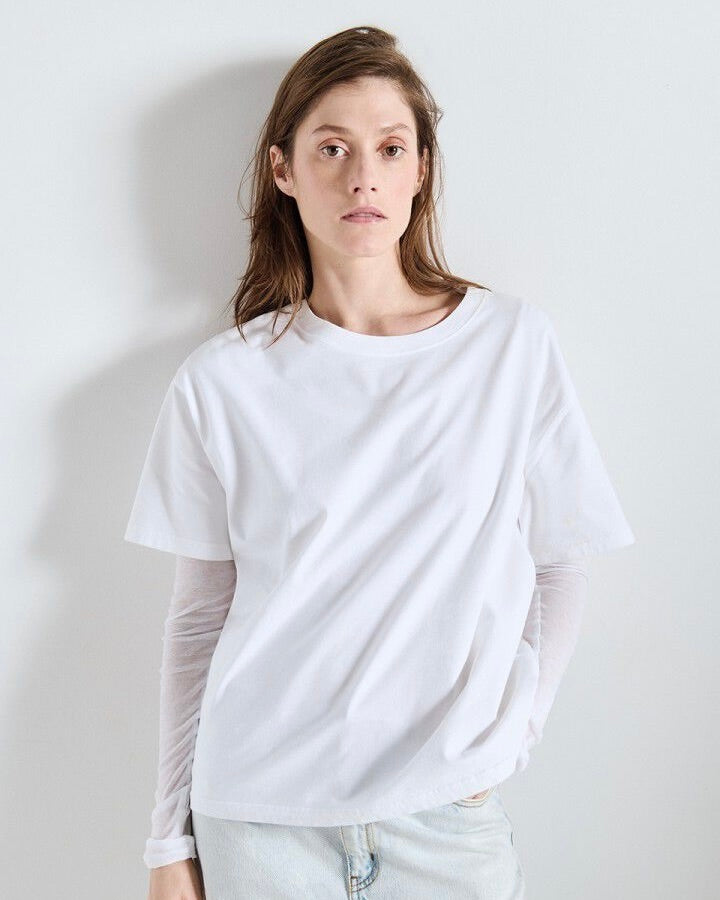Person wearing a white t-shirt with sheer sleeves against a plain background