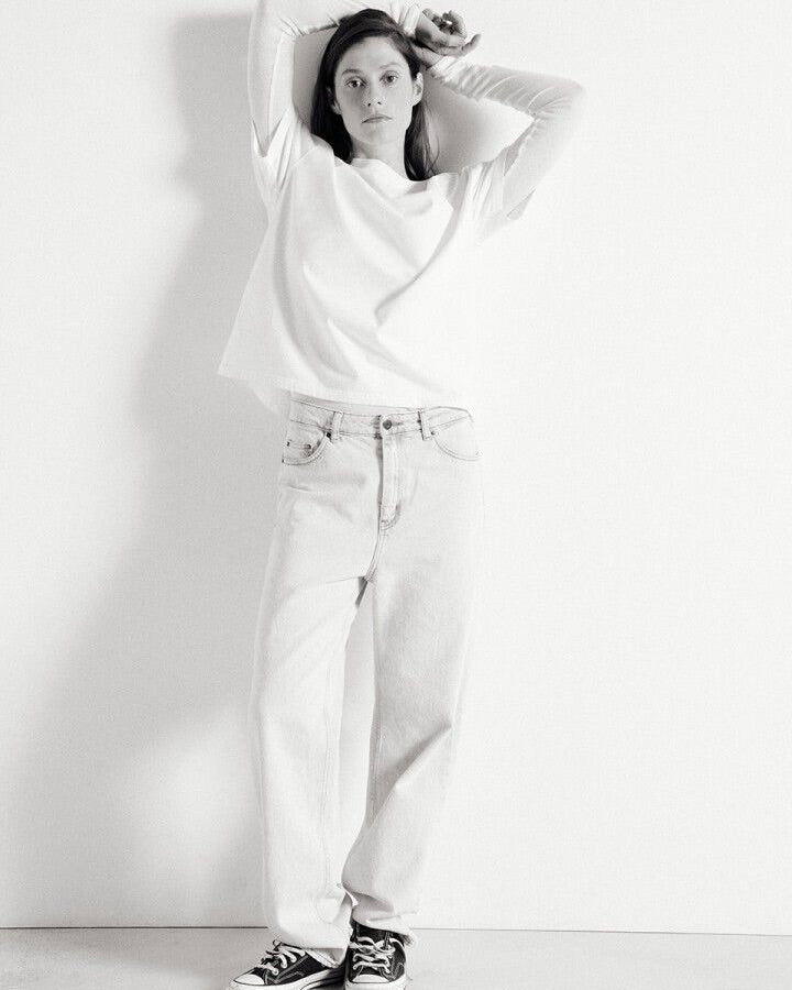 Person wearing a white top and light blue jeans against a plain background