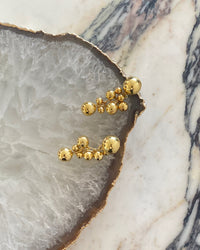 large bubble gold earrings rest on a crystal platter on marble