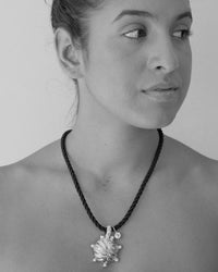 model wears a black cord necklace with an odd shaped metallic pendant