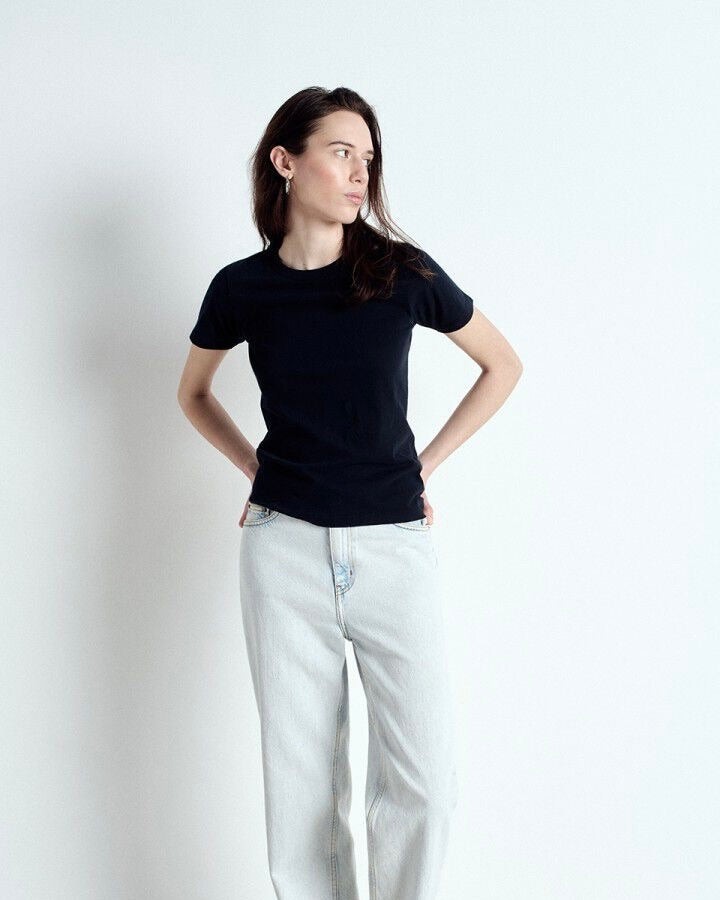 Woman wearing a black t-shirt and light blue jeans against a white background