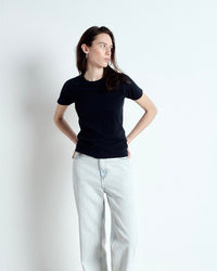 Woman wearing a black t-shirt and light blue jeans against a white background