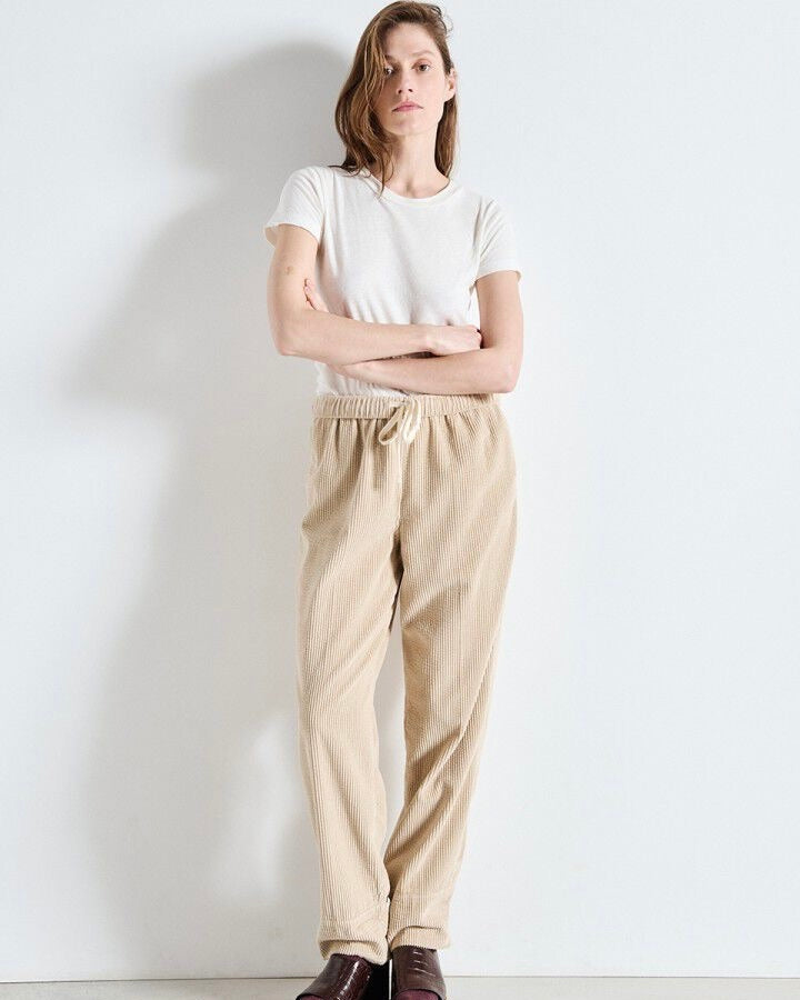 Woman wearing a white t-shirt and beige pants against a plain background