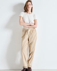 Woman wearing a white t-shirt and beige pants against a plain background