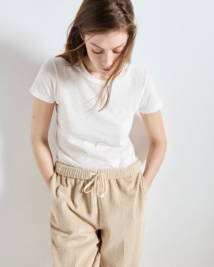 Person wearing a white t-shirt and beige pants against a plain background