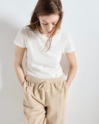 Person wearing a white t-shirt and beige pants against a plain background