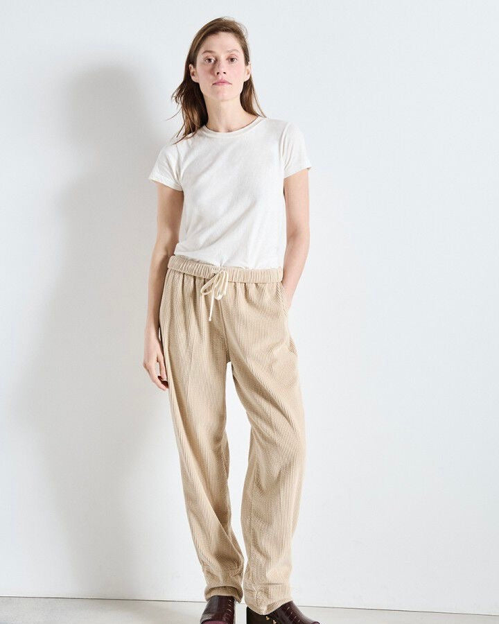 Woman wearing a white t-shirt and beige pants against a plain background