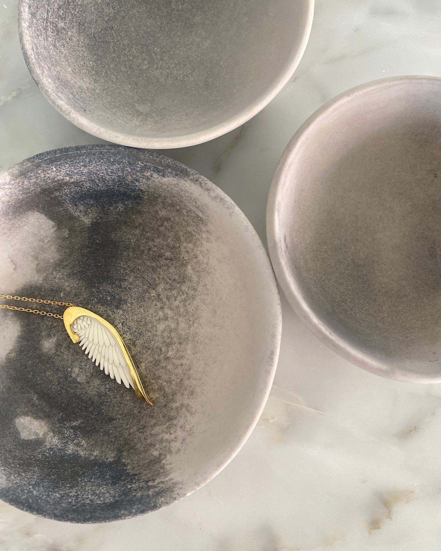 Long gold chain with a handcarved bone Wine pendant by Johnny Ramli sits in a bowl