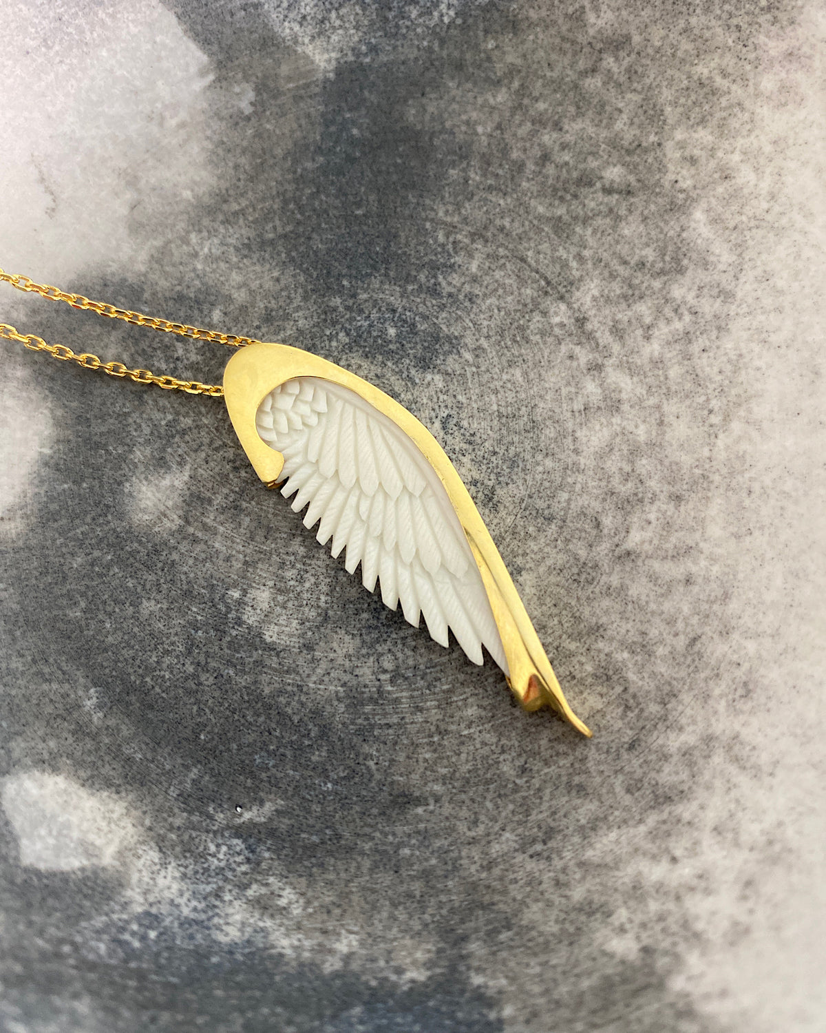 Long gold chain with a handcarved bone Wine pendant by Johnny Ramli sits on a mottled surface - available at the Pared Store