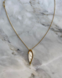 Long gold chain with a handcarved bone Wine pendant by Johnny Ramli sits on Marble