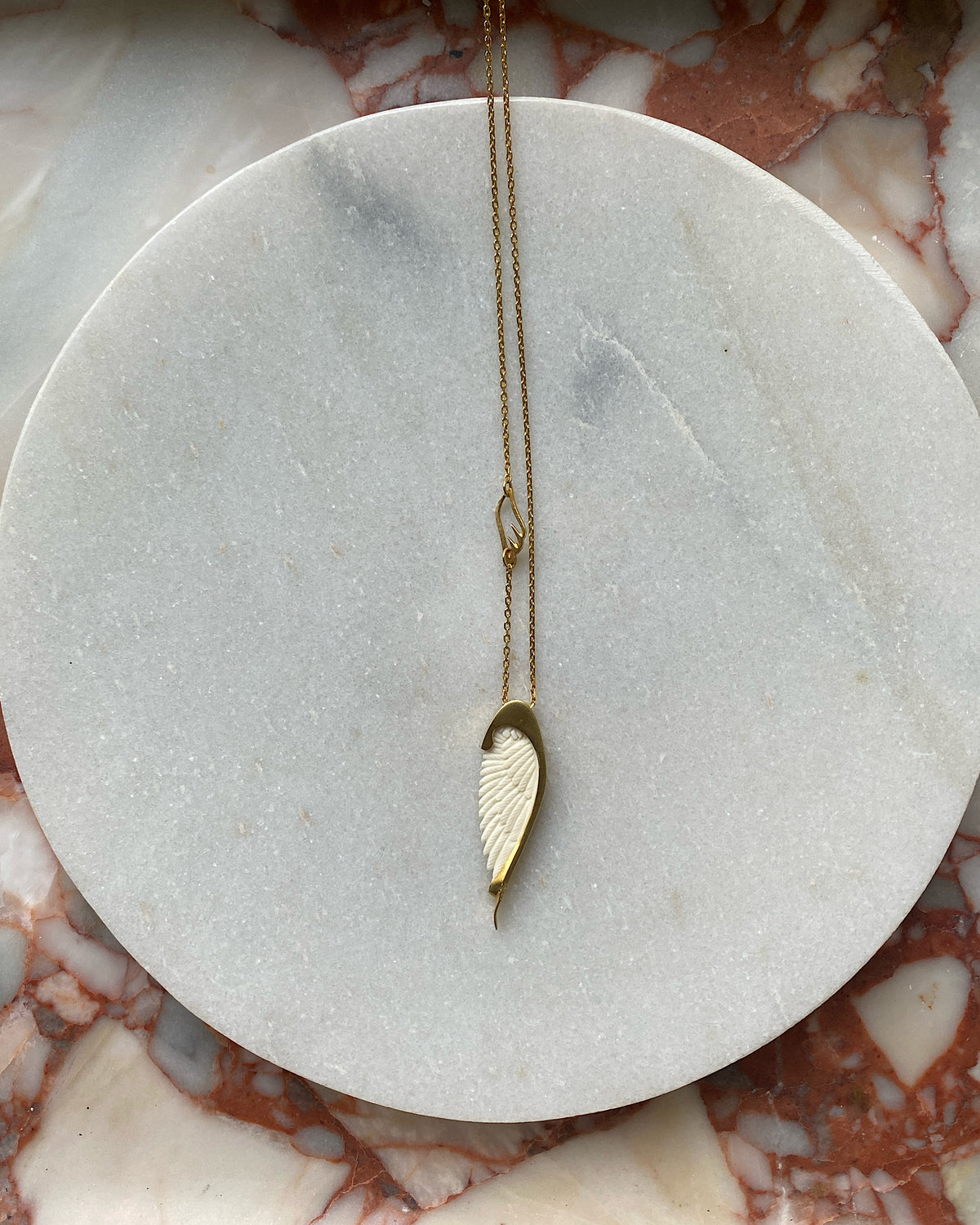 Long gold chain with a handcarved bone Wine pendant by Johnny Ramli sits on Marble