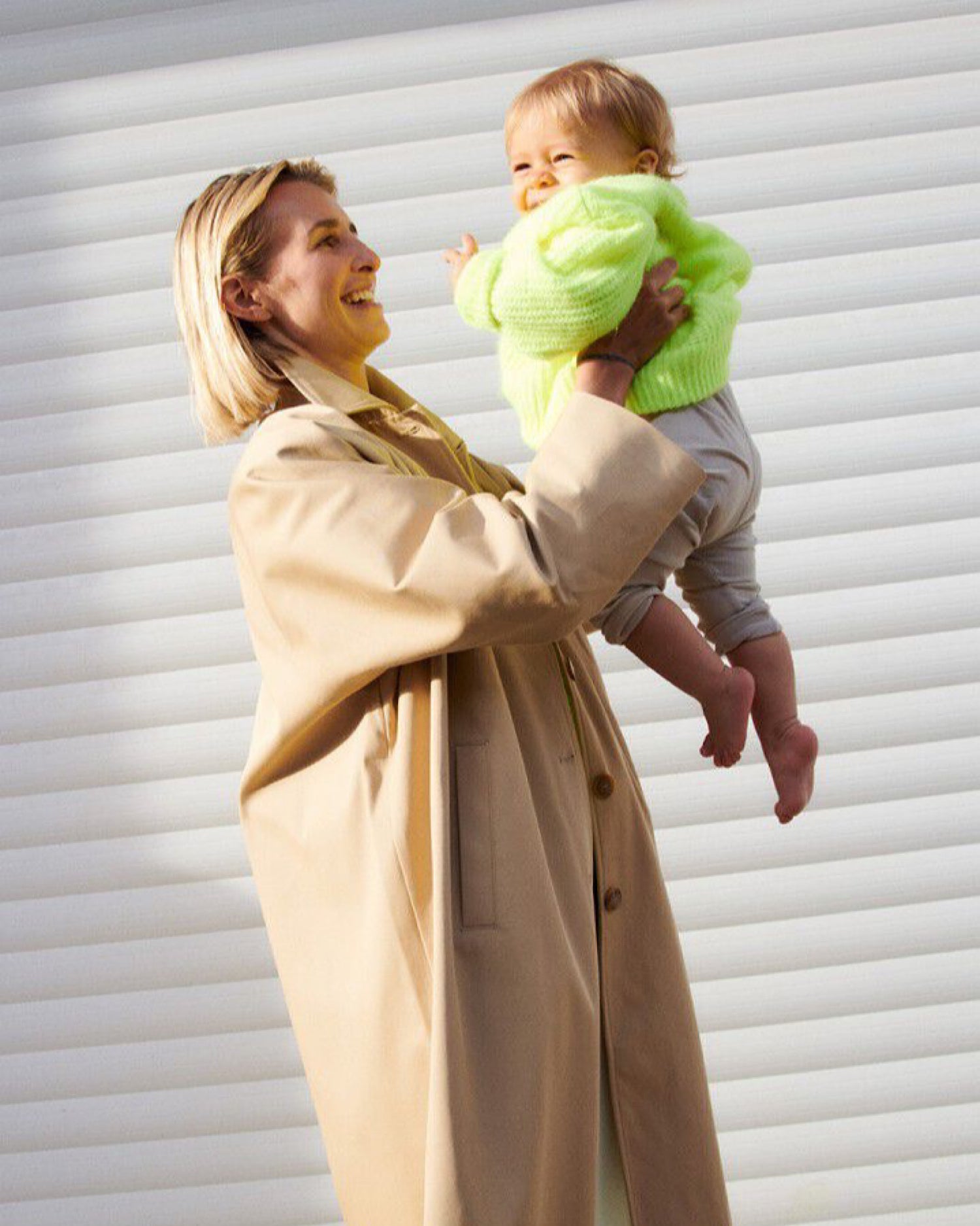 Woman holding a baby wrapped in green fabric against a white background