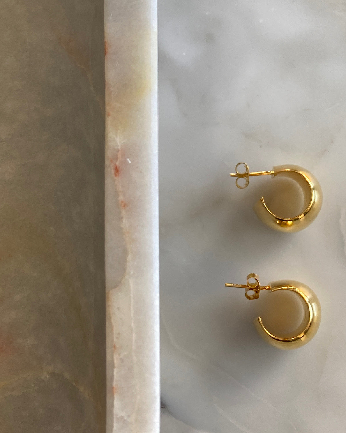 small gold wide hoop earrings on marble