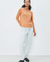 Person wearing a peach orange -colored boat neck long sleeve tee and light blue jeans on a white background