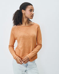 Woman wearing an orange long-sleeve boat neck top fro American Vintage against a plain background