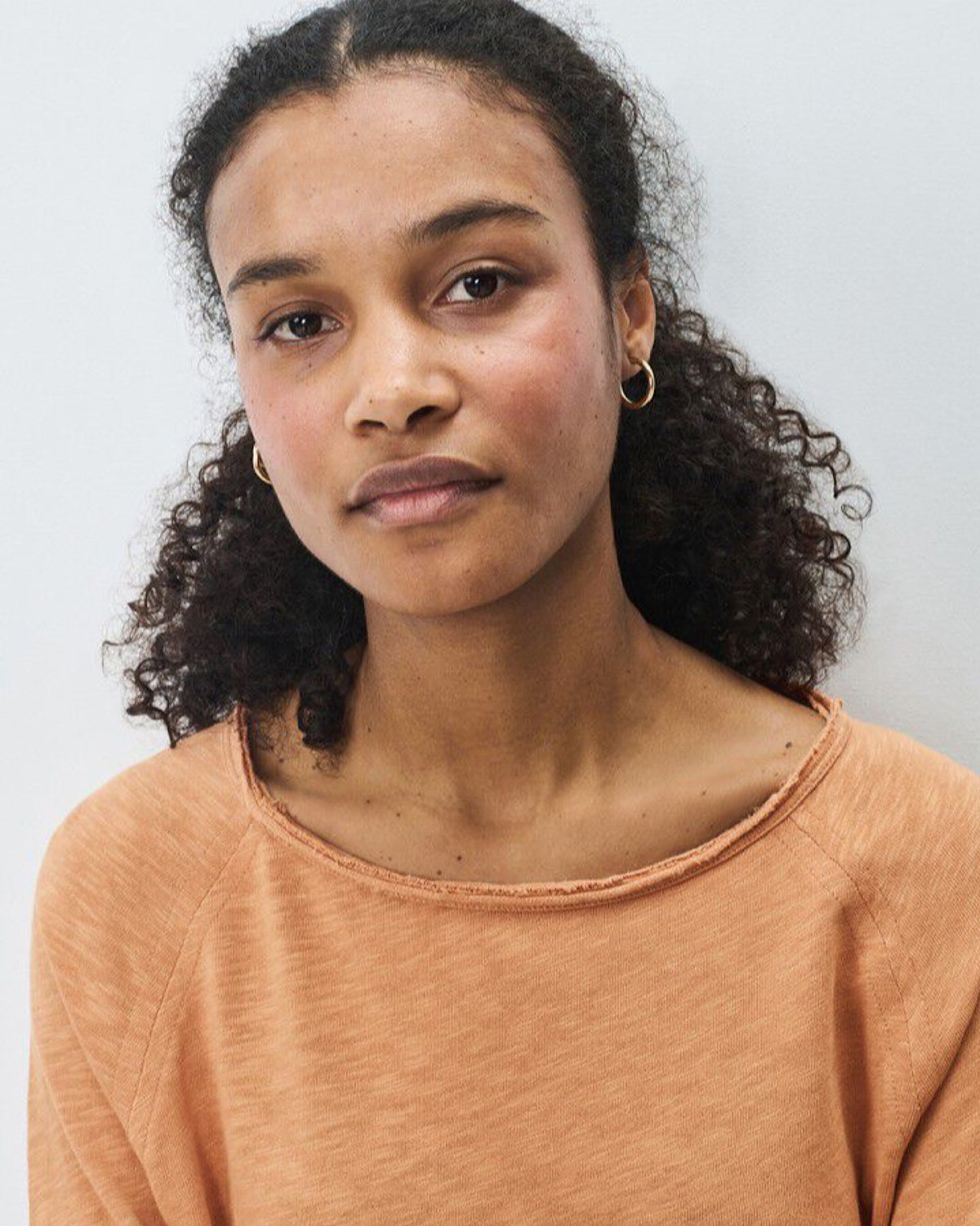 Woman wearing an tan orange tone top with a raw edge from American Vintage against a light background