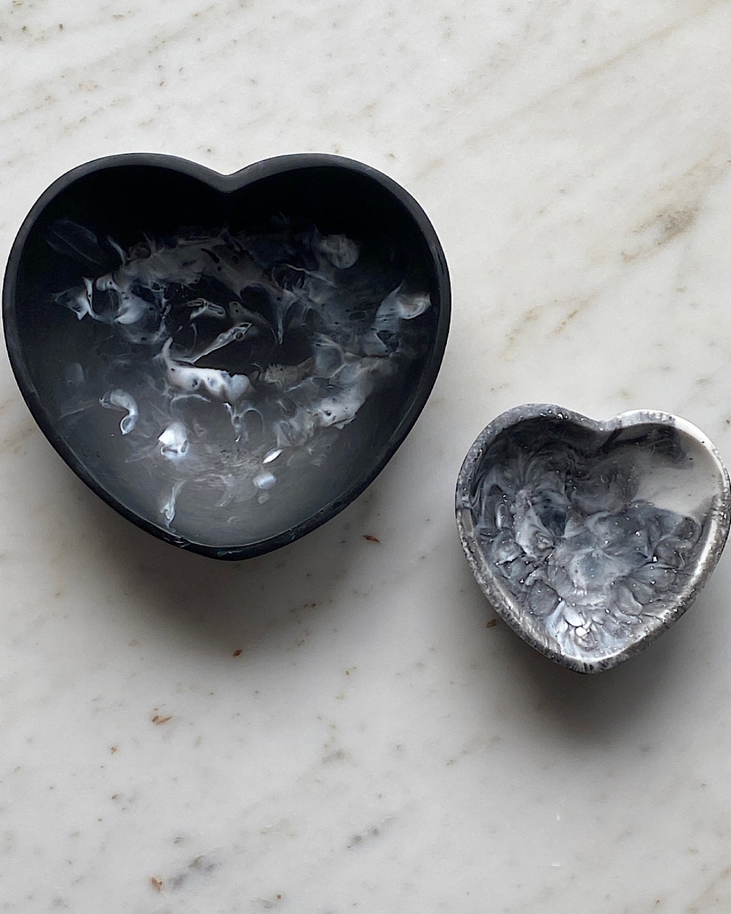 two black resin hearts sit on marble