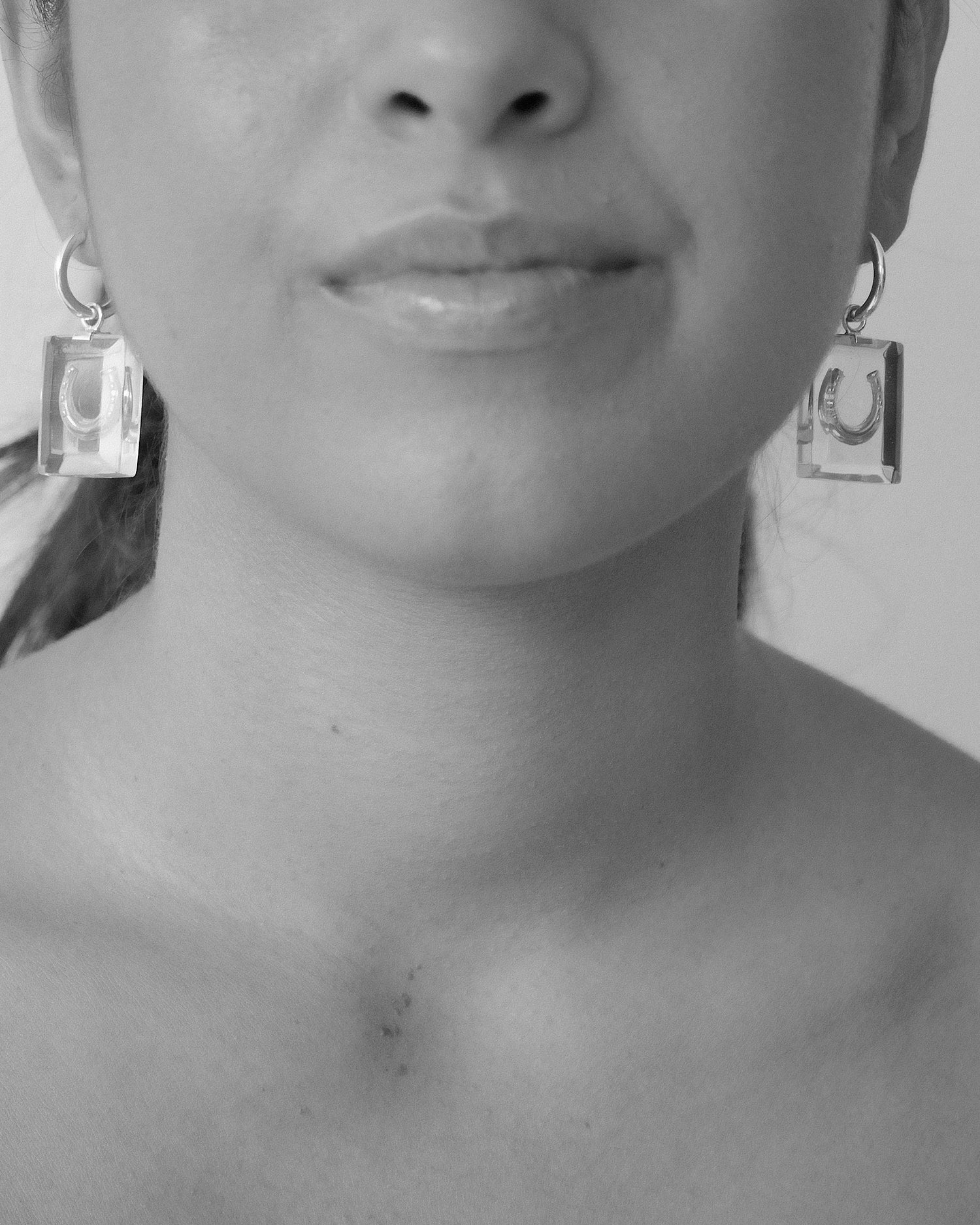 model wears hoop earring with clear resin rectangles on the bottom and a horse shoe charm suspended inside