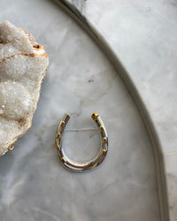 an oversized silver horseshoe brooch with gold accents sits on marb;e