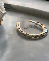 an oversized silver horseshoe brooch with gold accents sits on marb;e