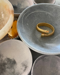 Striped wrap style gold cuff sits in a bowl